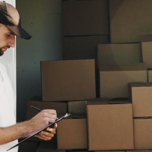 A photo showing a person holding a clipboard next to stacks of boxes. Consolidated shipping can be more complex than ordinary shipping.
