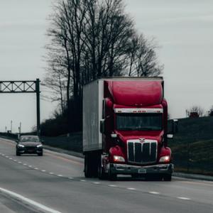 A photo showing a red truck driving on a highway on a cloudy day. A freight broker can match you with reliable freight carriers.